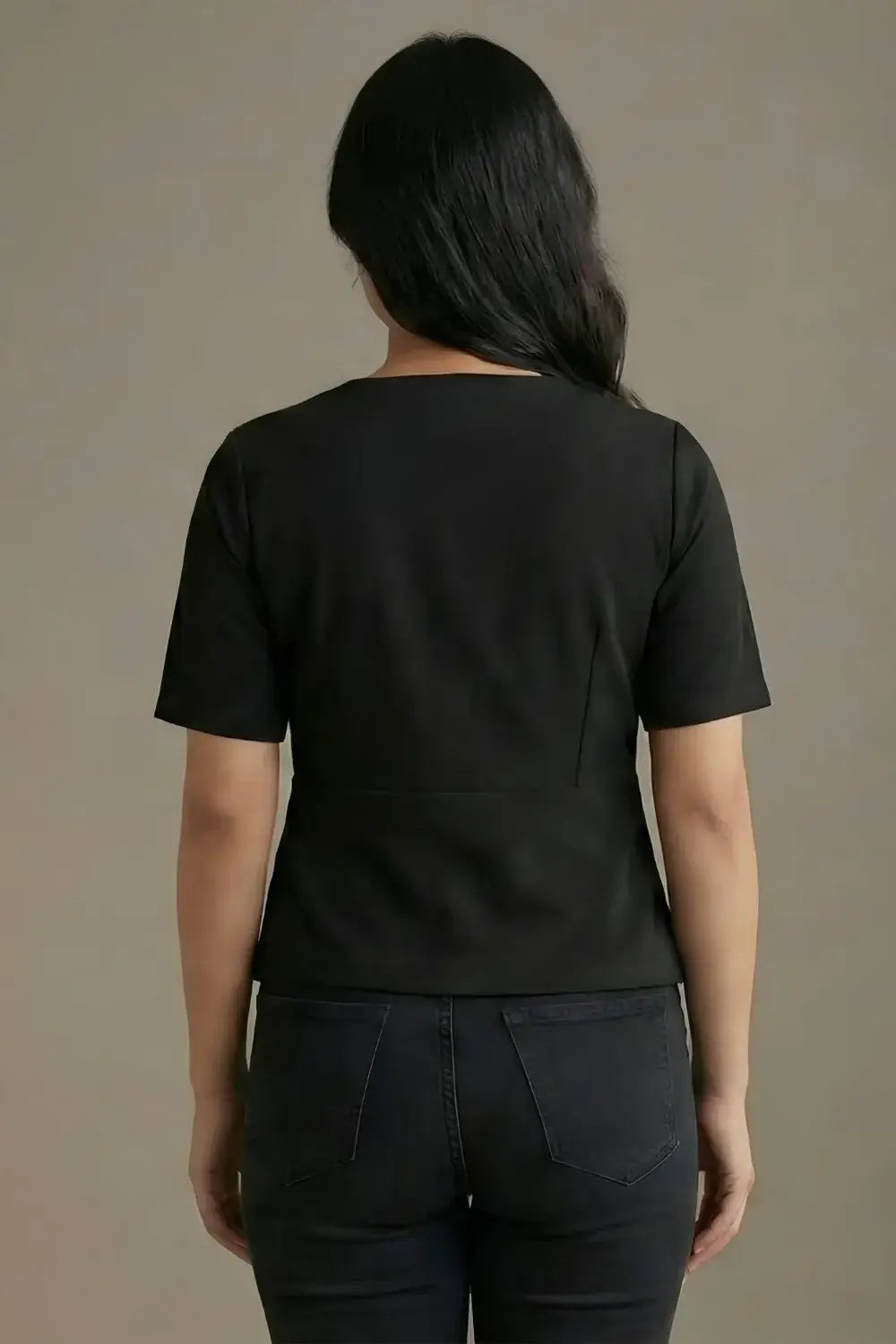 Person wearing a black t-shirt and dark pants against a beige background