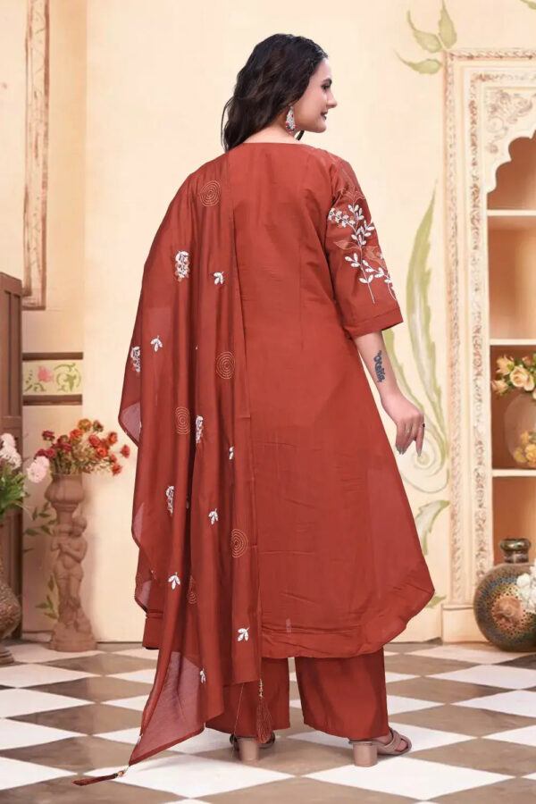 Woman wearing a rust-colored traditional outfit with floral patterns indoors.